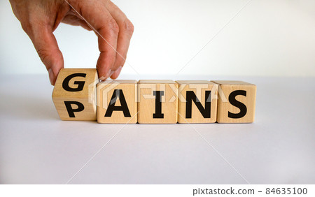 Gains and pains symbol. Businessman turns wooden cubes, changes word pains to gains. Beautiful white background. Business, pains and gains concept. Copy space. 84635100