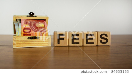 Concept word 'fees' on cubes on a beautiful wooden table, small chest with euro bills. Beautiful background. Copy space. Concept word 'fees' on cubes on a beautiful wooden table, small chest with euro bills. Beautiful background. Copy space. 84635163