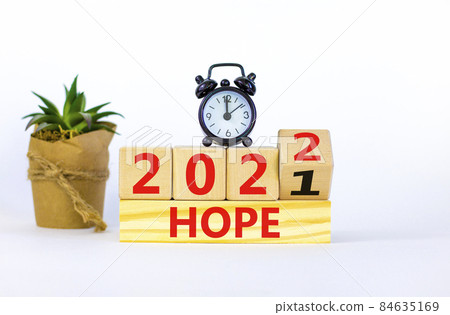 2022 hope new year symbol. Alarm clock. Turned a wooden cube, changed words 'Hope 2021' to 'Hope 2022'. Beautiful white background, copy space. Business, 2022 hope new year concept. 2022 hope new year symbol. Alarm clock. Turned a wooden cube, changed words 'Hope 2021' to 'Hope 2022'. Beautiful white background, copy space. Business, 2022 hope new year concept. 84635169