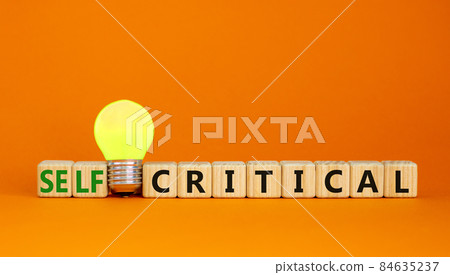 Critical or self-critical symbol. Cubes with words 'Self-critical or critical'. Yellow light bulb. Beautiful orange background. Psychology, critical or self-critical and business concept. Copy space. Critical or self-critical symbol. Cubes with words 'Self-critical or critical'. Yellow light bulb. Beautiful orange background. Psychology, critical or self-critical and business concept. Copy space. 84635237