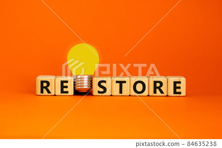 Restore symbol. Wooden cubes with the word 'restore'. Yellow light bulb. Beautiful orange background. Business and restore concept. Copy space. 84635238