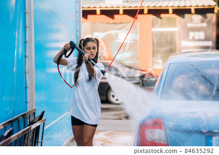 Brunette from a high-pressure hose washes the car at a car wash Brunette from a high-pressure hose washes the car at a car wash 84635292