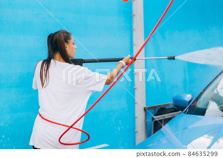 Brunette from a high-pressure hose washes the car at a car wash Brunette from a high-pressure hose washes the car at a car wash 84635299