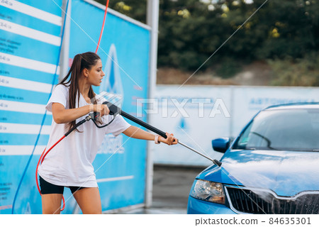 Brunette from a high-pressure hose washes the car at a car wash Brunette from a high-pressure hose washes the car at a car wash 84635301