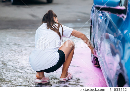 Brunette with two pigtails with a sponge washes the side of the car Brunette with two pigtails with a sponge washes the side of the car 84635312