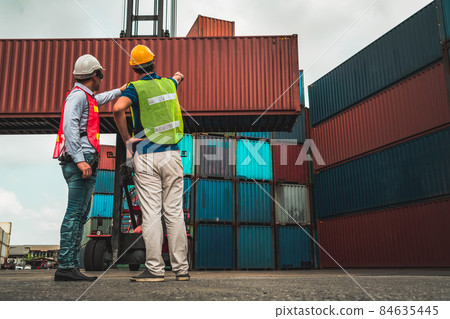 Industrial worker works with co-worker at overseas shipping container yard 84635445