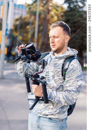 Professional videographer with gimball doing video equipment setup before shooting. He is balancing camera Professional videographer with gimball doing video equipment setup before shooting. He is balancing camera 84635984
