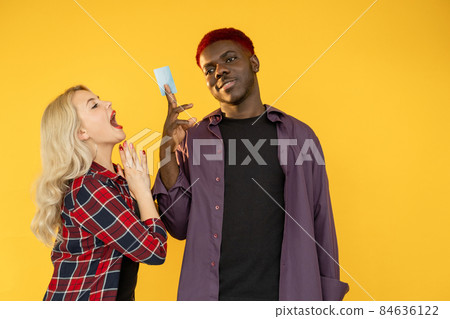 Couple budget. Greedy shopaholic. Family income. Gold digger. Multicultural pair of excited white woman begging for credit card money to Afro man isolated on orange free space. Couple budget. Greedy shopaholic. Family income. Gold digger. Multicultural pair of excited white woman begging for credit card money to Afro man isolated on orange free space. 84636122