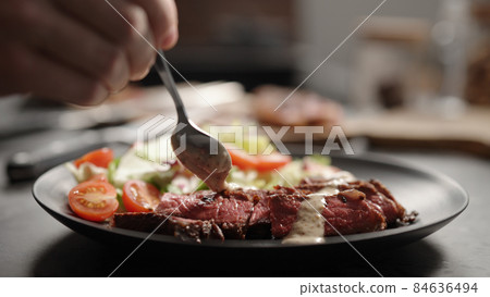 man pour pepper or nut sauce on slices of new york steak on plate with mixed vegetables 84636494