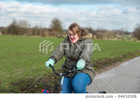 Tienen, Flanders / Belgium - 07 20 2018: Portrait of a young white woman with Down Syndrome driving a tricycle through the fields Tienen, Flanders / Belgium - 07 20 2018: Portrait of a young white woman with Down Syndrome driving a tricycle through the fields 84638306