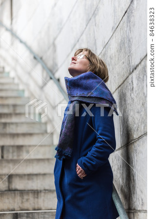 Portrait of a 30 yo woman, blue coat and scarf looking up with a grey stone wall and stair background Portrait of a 30 yo woman, blue coat and scarf looking up with a grey stone wall and stair background 84638323