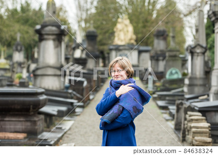 Portrait of a thirty year old woman with a blue winter coat and scarf at a cemetery Portrait of a thirty year old woman with a blue winter coat and scarf at a cemetery 84638324
