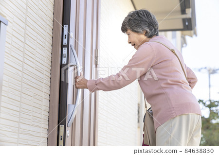 Senior woman holding the handle of the front door of a house Senior woman holding the handle of the front door of a house 84638830