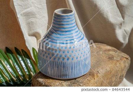 White and Blue handmade ceramic vase on white textured table cloth. White and Blue handmade ceramic vase on white textured table cloth. 84643544
