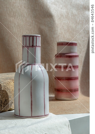 Two white and pink handmade ceramic vases on white textured table cloth. Two white and pink handmade ceramic vases on white textured table cloth. 84643546