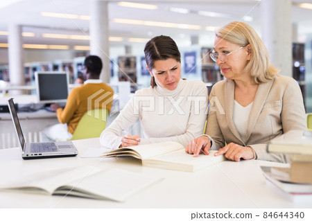 Female teacher working with girl student in university library Female teacher working with girl student in university library 84644340