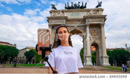 Travel influencers Milan island. Paint building house in Europe Milano. Photographer blogger girl with smartphone in Piazza del Duomo, Cathedral Square. Traveling and freelancing, modern lifestyle. 84645049