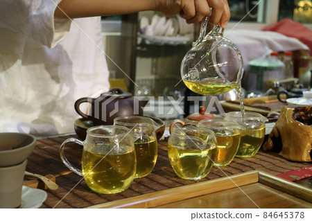 有人正在泡茶葉 並用透明的茶壺倒出一杯杯茶飲 84645378