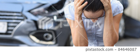 Frightened woman sits in front of wrecked car closeup 84646087