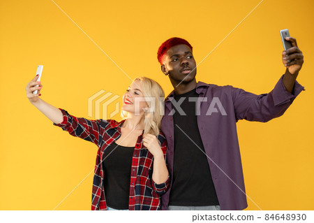 Phone selfie. Blog lifestyle. Modern technology. Multiracial friendship. Multiethnic African man Caucasian woman friends posing taking cell photo isolated on orange background. 84648930
