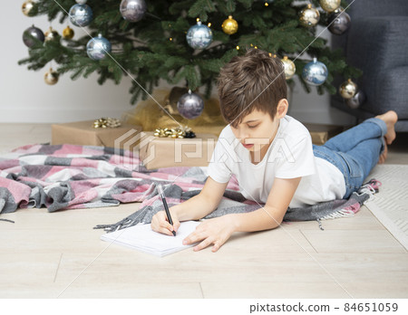 Boy writes letters to Santa Claus near the Christmas tree Boy writes letters to Santa Claus near the Christmas tree 84651059