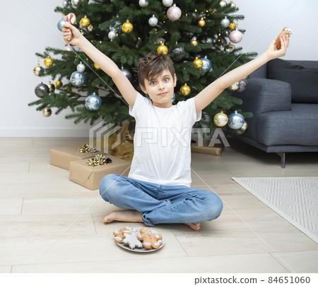 Boy eating Christmas gingerbread near the Christmas tree Boy eating Christmas gingerbread near the Christmas tree 84651060