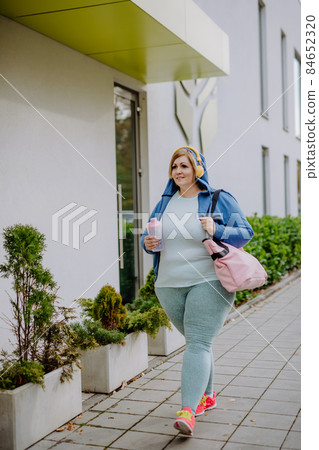 Happy overweight woman in sports clothes outdoors on the way to fitness center Happy overweight woman in sports clothes outdoors on the way to fitness center 84652320