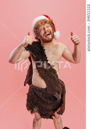 Portrait of cheerful man in character of neanderthal wearing animal skin cloth joyfully posing isolated over pink background 84652328