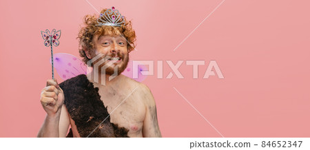 Cropped portrait of cheerful happy man in character of neanderthal wearing little fairy crown isolated over pink background 84652347