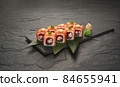 sushi rolls with tuna salmon eel unagi and avocado on a black stone plate. 84655941
