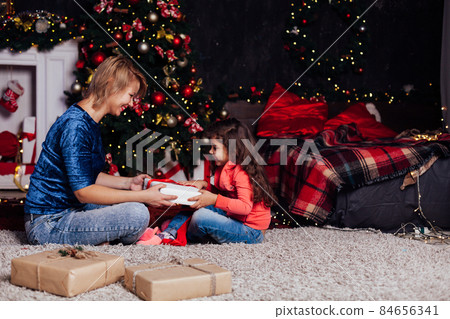 mom little girl opens gifts at the Christmas tree new year 84656341