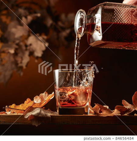 Whiskey is poured into a glass with ice. 84656484