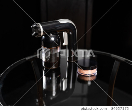 A close-up of the instant tanning equipment. Gun spraying paint for leather and matting body powder on a black background A close-up of the instant tanning equipment. Gun spraying paint for leather and matting body powder on a black background 84657375