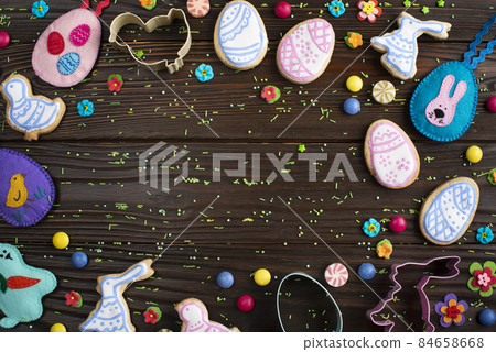 Cookie cutters, felt toys and Easter frosted cookies in shape of egg, chicken and rabbit on dark wooden background fat lay view. 84658668