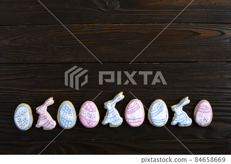 Easter frosted cookies in shape of egg and rabbit on dark wooden background. Flat lay with copy space. Easter frosted cookies in shape of egg and rabbit on dark wooden background. Flat lay with copy space. 84658669