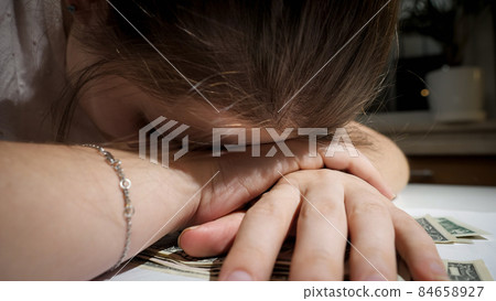 Closeup of stressed worried woman lying on kitchen table and piley of money banknotes 84658927