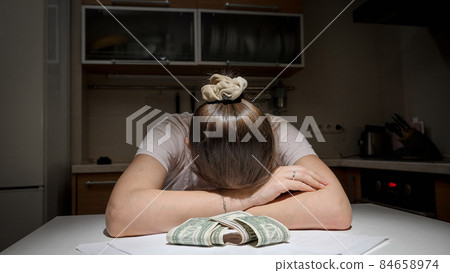 Stressed woman having to pay rent and bank loan lying on kitchen next to few money banknotes 84658974