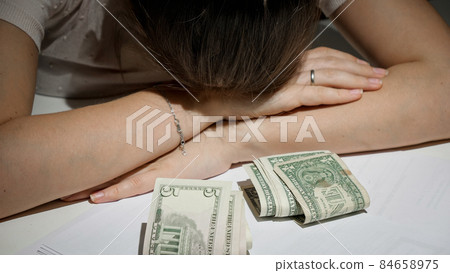 Stressed woman with big debt and financial problems lying on table next to few money banknotes Stressed woman with big debt and financial problems lying on table next to few money banknotes 84658975