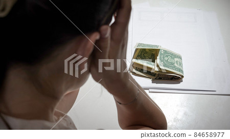 Stressed woman sitting behind desk and looking on few money banknotes to pay rent loan Stressed woman sitting behind desk and looking on few money banknotes to pay rent loan 84658977
