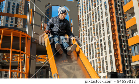 Happy smiling boy riding down slide on modern children playground Happy smiling boy riding down slide on modern children playground 84659818