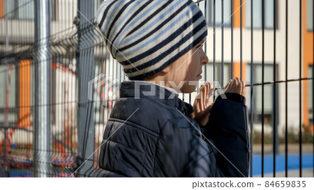 Upset and stressed boy looking through school metal fence after was bullied. Concept of poverty, immigration, bullying and kids stress 84659835
