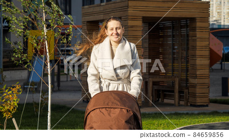 Smiling young mother walking with her baby in stroller outdoors at park 84659856