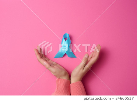 woman hands holding light blue ribbon awareness on a pink background. Men's health and prostate cancer awareness campaign concept. woman hands holding light blue ribbon awareness on a pink background. Men's health and prostate cancer awareness campaign concept. 84660537