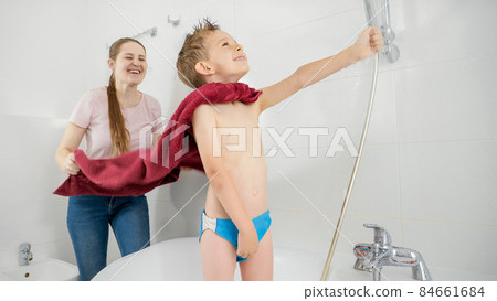 Funny smiling boy with mother playing in superhero while washing under shower in bathroom. Concept of family time, children development and fun at home 84661684
