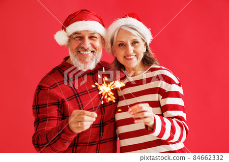 Happy overjoyed senior family couple in Santa hats with Bengal sparkler light celebrate New year Happy overjoyed senior family couple in Santa hats with Bengal sparkler light celebrate New year 84662332