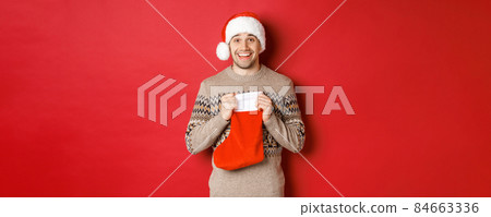 Concept of winter holidays, new year and celebration. Image of surprised and happy man receiving gift from secret santa inside christmas stocking bag, open gift and looking thankful 84663336