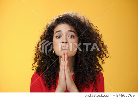 Please I beg you. Portrait of sad and cute curly-haired girl with angel eyes pouting holding hands in pray and looking hopeful at camera waiting for mercy asking apology, supplicating over yellow wall 84663769