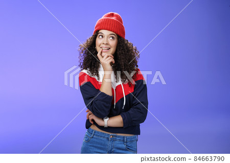 Girl making up idea what snowman built standing cute and silly with thoughtful expression biting finger as thinking, smiling delighted, having interesting thought standing in hat and warm sweatshirt Girl making up idea what snowman built standing cute and silly with thoughtful expression biting finger as thinking, smiling delighted, having interesting thought standing in hat and warm sweatshirt 84663790