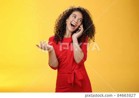 Talkative glamour silly girl with curly hair having fun feeling carefree and happy taling on mobile phone turning away as laughing joyfully gesturing with hand holding smartphone pressed to ear Talkative glamour silly girl with curly hair having fun feeling carefree and happy taling on mobile phone turning away as laughing joyfully gesturing with hand holding smartphone pressed to ear 84663827