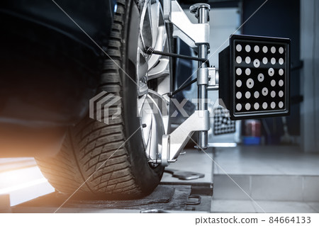 CLose-up car wheel indoors service maintenance repair center against laser sensor equipment diagnostics and 3d wheel alignment. Vehicle inside garage workshop for auto camber toe check fixing work CLose-up car wheel indoors service maintenance repair center against laser sensor equipment diagnostics and 3d wheel alignment. Vehicle inside garage workshop for auto camber toe check fixing work 84664133